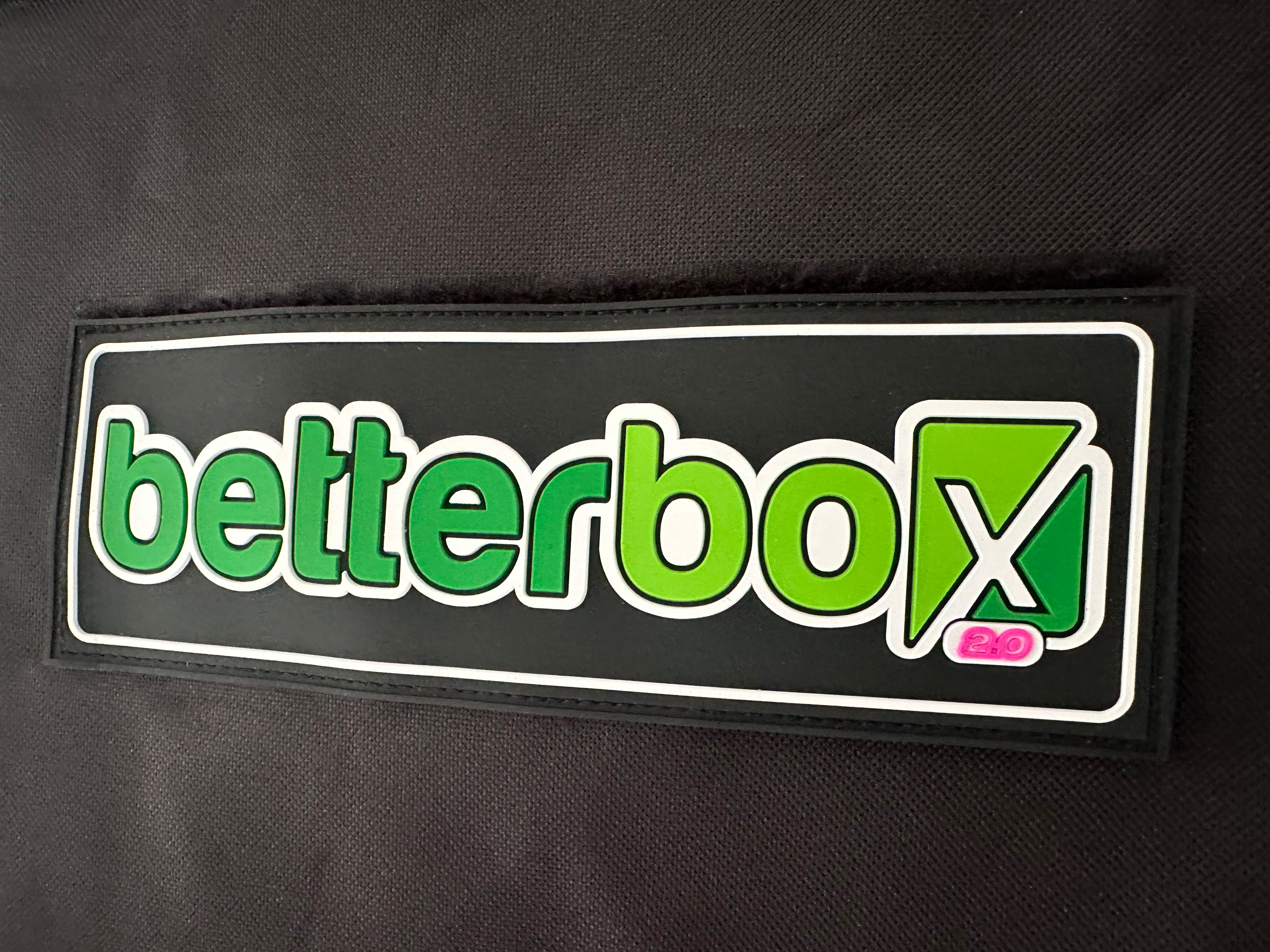 Betterbox-2.0-Logo mit pinkem Versionszeichen auf schwarzem Stoff